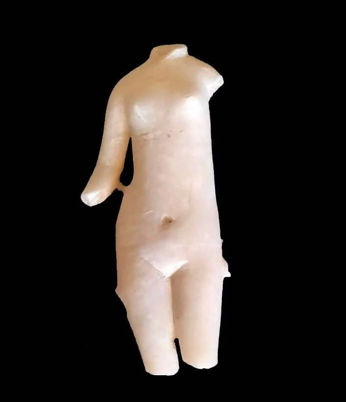 A small white marble statue with one arm stands against a black background.